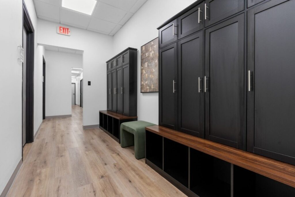 Ikon-09374-2048x1365 Hallway with black cabinets, wooden benches, green stool, and exit sign.