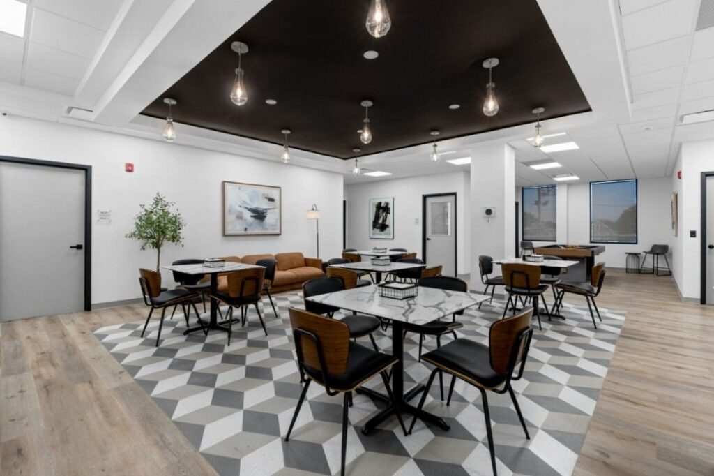 Ikon-11-2048x1365 Modern lounge with geometric floor, tables, chairs, and leather couch under pendant lights.