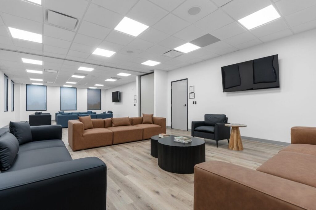 Ikon-16-2048x1365 Modern lounge with brown and black sofas, round tables, and a mounted TV on the white wall.