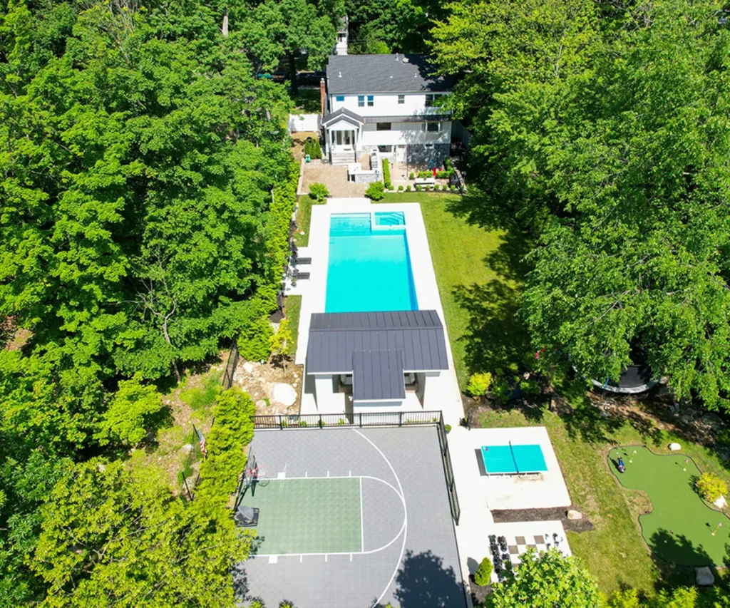 newlifementalhealthnj Aerial view of a house with pool, basketball court, and surrounding green trees.